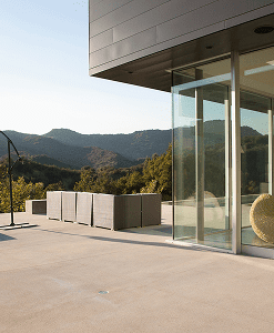 Modern patio with glass walls, outdoor seating area, and mountain view in the background under clear skies.