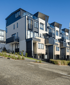 Row of modern, multi-story townhouses with balconies on a sloped street under a clear blue sky.
